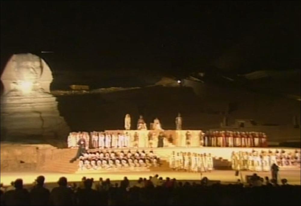 Il video è parte di “Attraverso lo spettacolo”, collezione che raccoglie le risorse digitali di “Attraverso lo spettacolo - Archivio ipermediale italo­greco in rete” progetto nato nel 2008 dalla collaborazione fra la Regione Puglia e la Grecia, che ha reso disponibili nelle biblioteche in terra ellenica e pugliese i dvd di ben 76 spettacoli artistici. Siamo dinanzi alla celebre opera di Giuseppe Verdi, l'Aida, che la produzione del Teatro Petruzzelli nel 1986 riuscì a portare in scena nel suo palcoscenico naturale, ovvero la vallata di Gyza, nel Cairo. In un'area di oltre 4000 mq le maestranze del teatro Petruzzelli lavorarono con la manodopera locale per allestire le scenografie di Tito Varisco, il palcoscenico, la vastissima platea, per organizzare il sistema di ampli...