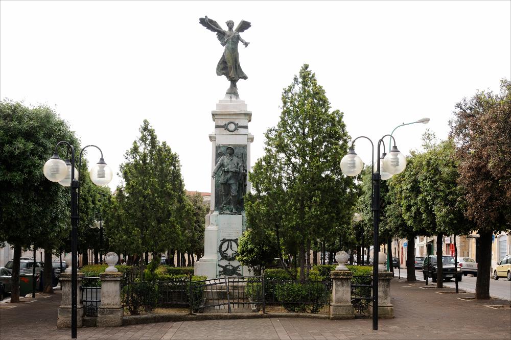 L'immagine digitale riproduce il Monumento ai Caduti di Bitetto. Datato al 1921, è opera dell'artista Giuseppe Tonnini, scultore nato a Loreto e attivo a Roma, che si specializzò nelle commissioni di sculture pubbliche a carattere celebrativo, uno dei collaboratori della parte di ornamentazione del Vittoriano. A Bitetto, un'esile figura femminile alata, leggera e dalle forme aggraziate svetta su un basamento quadrangolare che riporta nella parte anteriore, in basso, la figura di un fiero soldato equipaggiato, nell'atto di camminare, che mostra la targa dedicatoria dei Caduti. Lo stesso artista aveva realizzato il monumento di Modugno, non più in loco e rifatto negli anni '60 da De Bellis.