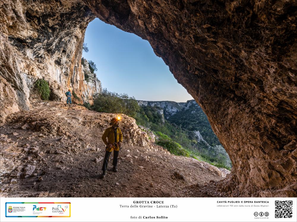 Un panorama mozzafiato dall’ingresso della Grotta Croce 1, dominato da una imponente volta alta 9 metri,  che si affaccia sulla Gravina di Laterza. Dopo il buio delle grotte finalmente la luce che fa apprezzare la bellezza naturalistica di questi paesaggi ancora inesplorati.
L’immagine digitale fa parte della raccolta di fotografie prodotte da Carlos Solito per il Progetto digitale “Sillabario sotterraneo – Viaggio dantesco nelle Grotte di Puglia” – realizzato nell’ambito della LEGGE REGIONALE 30 dicembre 2020 - art. 39 “Cavità pugliesi e opera dantesca - Celebrazioni 700 anni dalla morte di Dante Alighieri”.