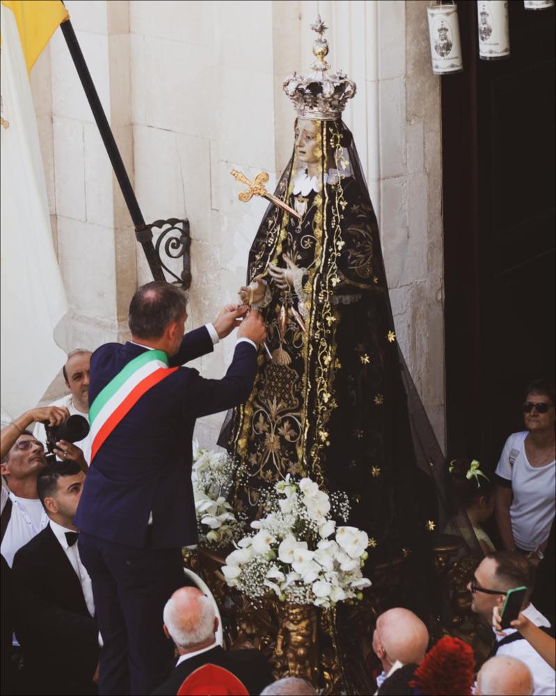 <div class="ql-editor"><div>L'immagine digitale immortala un momento solenne della Festa Patronale in onore di Maria SS. Addolorata di Mola di Bari (Ba): il rito della "consegna delle chiavi", in cui è il Sindaco che consegna simbolicamente le chiavi della città alla statua di Maria SS. Addolorata. Questo gesto, che sancisce l'atto di affidamento dell'intera comunità molese alla sua Patrona, si svolge davanti alla Chiesa della Maddalena, sul sagrato o nei pressi della chiesa prima dell'avvio della solenne Processione di Gala.</div><div>La Festa Patronale in onore di Maria SS. Addolorata, la cosiddetta “Festa Grande”, è uno degli eventi più importanti della vita religiosa e sociale della comunità. Celebrata ogni anno nell...