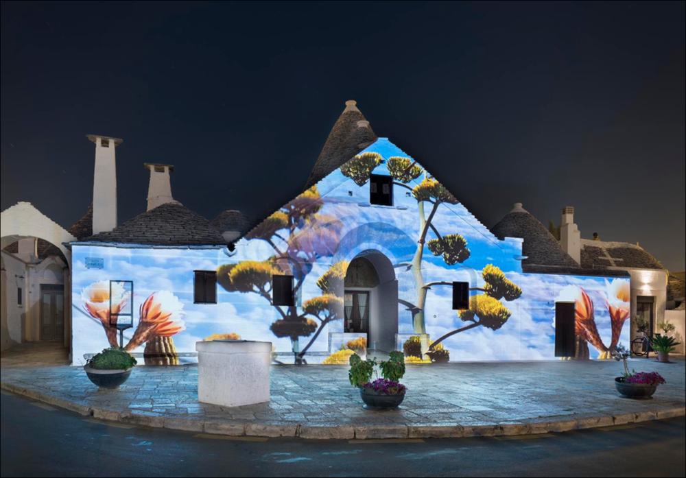 Lo scatto fotografico riprende la video installazione “Quintessenza”, opera dell'Associazione Lightcones.
La video installazione italiana ha trasformato il Trullo Sovrano di Alberobello, giocando con luci e suoni, i cinque solidi platonici e il loro rapporto con gli ambienti naturali.
In quest’opera Lightcones riprende il pensiero di Platone che, nel “Timeo”, tratta le origini e il funzionamento del cosmo, ipotizzando che la materia sia composta da quattro particelle fondamentali aventi la forma dei primi quattro poliedri regolari e corrispondenti ai quattro elementi tradizionali, a cui si aggiunge il concetto di “quintessenza” che racchiude il quinto elemento, l’universo.
L’installazione è stata realizzata nell’ambito della seconda edizione del Life - Alberobello Light...