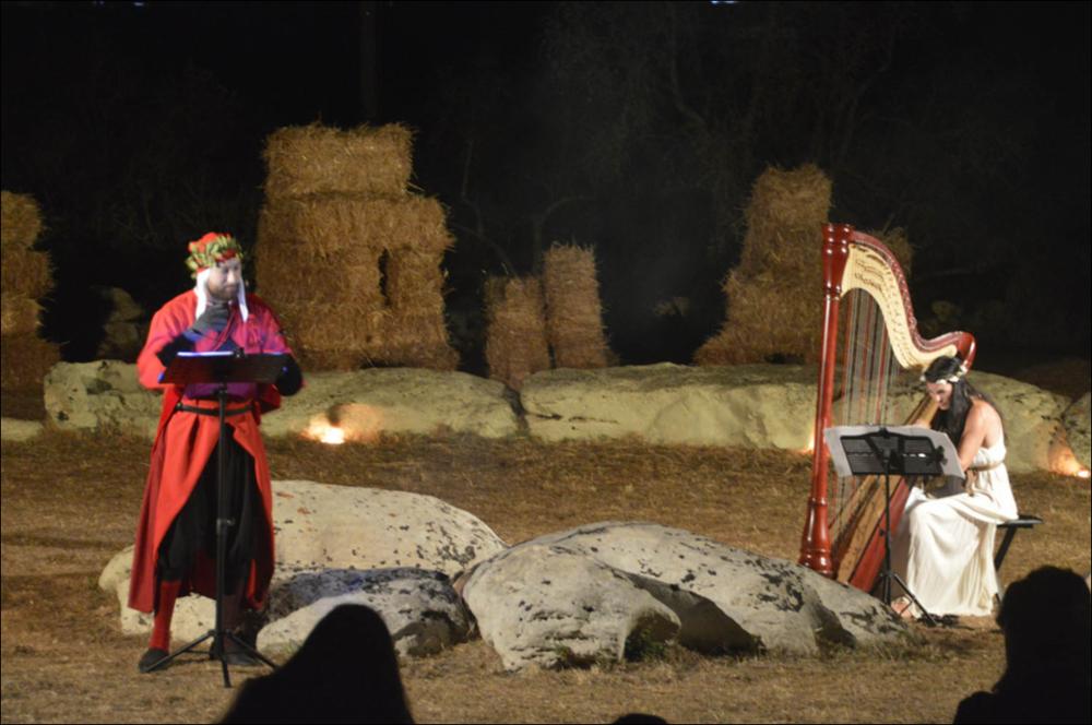 Lo scatto fotografico riprende un momento della performance dell’attore Andrea Sirianni e della musicista d’arpa Angela Cosi, durante la seconda edizione del “Dolmen Festival” 2021. L’attore porta in scena una lettura teatralizzata di alcuni dei più celebri passi dell’Inferno, dalla Divina Commedia di Dante, per celebrare i 700 anni dalla morte del “Sommo” poeta.
La suggestiva location dello spettacolo è località Dolmen “Lì Scusi”, uno dei luoghi simbolo per la storia dell’area di Minervino di Lecce, nota per le sue costruzioni megalitiche tra le più rappresentative della Puglia....