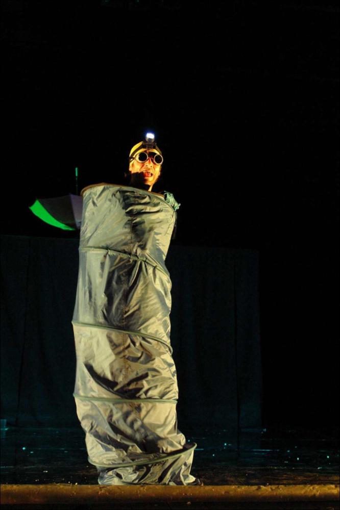 La fotografia in oggetto, ad opera di Bigsur, immortala un momento dello spettacolo “Giardini di Plastica”, una delle produzioni 2015-2016, dedicate al teatro per ragazzi, messe in scena dalla compagnia teatrale Koreja di Lecce. Lo spettacolo, sotto la regia di Salvatore Tramacere, permette al pubblico di viaggiare attraverso mondi fantastici e colorati, mondi abitati da tre personaggi camaleontici, ora extraterrestri, ora samurai, fate o angeli. I costumi e gli oggetti di scena provengono tutti dalla nostra quotidianità ma sul palco acquisiscono nuova vita: bacinelle diventano astronavi, cannucce e mollette servono per abbellire i vestiti, tappi di plastica usati come parrucche. Un solo personaggio è sulla scena di questa fotografia, travestito forse da un bruco.