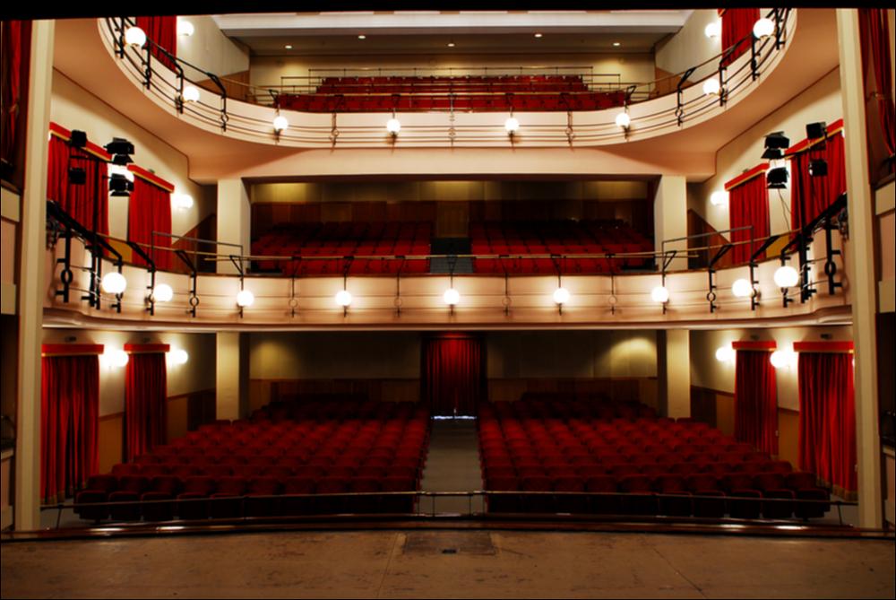 L'immagine è parte della campagna fotografica realizzata dalla fotografa Margherita Mirabella per Teatro Pubblico Pugliese, che ha ripreso nei suoi scatti le eleganti architetture e i rifiniti dettagli di alcuni dei più bei teatri pugliesi e alcuni degli spettacoli teatrali portati in scena in questi ultimi anni. L'autrice cattura il prospetto principale di Teatro Saverio Mercadante, situato in Piazza Giacomo Matteotti a Cerignola. Oggi gestito in collaborazione con il Teatro Pubblico Pugliese, la struttura teatrale fu inaugurata nel 1868. La storia del teatro inizia nel 1854, quando fu proposta la necessaria costruzione di un teatro cittadino. Dopo diverse proposte che risultarono piuttosto onerose, la scelta ricadde sull'architetto Leopoldo Vaccaro, che presentò un pr...