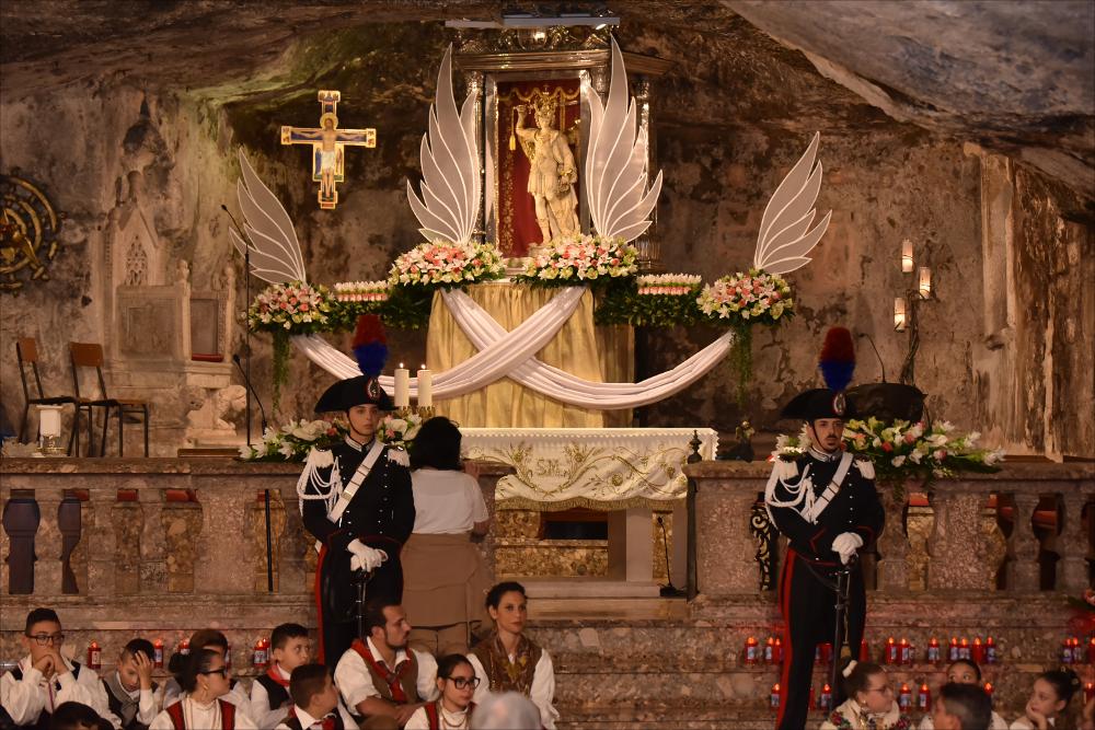 L’immagine ritrae l’altare della Basilica Santuario di San Michele Arcangelo e, sullo sfondo, la statua devozionale del Santo Patrono che reca in mano la Sacra Spada.
Il “Rito della Sacra Spada” viene celebrato il 29 settembre all’interno della Grotta del Santuario e presieduto dal vescovo. Durante la cerimonia la spada viene estratta dalla statua, gesto fortemente simbolico che richiama la Parola di Dio capace di distinguere il bene dal male e di offrire protezione e guarigione spirituale ai fedeli. La reliquia viene poi portata in processione come segno di devozione e di affidamento.
La festa patronale di Monte Sant’Angelo, dedicata a San Michele Arcangelo e celebrata il 29 settembre con riti che si estendono nei giorni precedenti e successivi, è tra gli eventi religi...