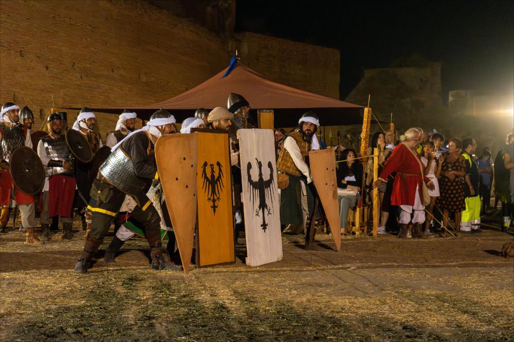 <div><strong>Schieramento angioino durante il Villaggio Medioevale di Lucera 2025.</strong></div><div>La scena è tratta da <em>“Corradino e la rivolta nel regno”</em>, primo episodio della rievocazione storica <em>“1268-1269 – L’assedio angioino di Lucera”</em>, organizzata e coordinata dall’APS Cinque Porte Storiche – Città di Lucera, con direzione scientifica e partnership dell’Associazione storico-culturale <em>Imperiales Friderici II</em> di Foggia, in collaborazione con l’Archeoclub d’Italia – sede di Lucera “Minerva” e con la partecipazione di associazioni italiane di living history e re-enactment del Duecento.</div><div>La rievocazione ricostruisce le fasi dell’ass...