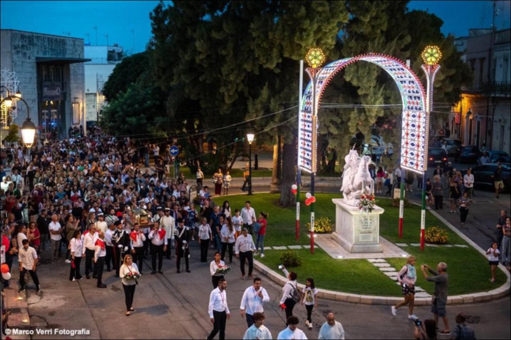 Questo scatto fotografico del 2022 immortala Piazza Risorgimento a Melendugno, dove troneggia la statua di San Niceta il Goto, gremita di gente in festa che celebra la Festa in onore del Santo Patrono.
La Festa Patronale di San Niceta Goto Martire, istituita nel 1740, si celebra nei giorni 15 e 16 Settembre a Melendugno in provincia di Lecce. Il rito religioso parte nove giorni prima della Festa, con delle celebrazioni eucaristiche presso la chiesa Madre e in forma esclusiva viene celebrata la santa messa in rito bizantino presso l’Abbazia di San Niceta situata in Melendugno sin dal 1167, riconosciuta appunto come uno dei più importanti riferimenti storici del territorio.
Il giorno della vigilia della Festa, come da tradizione pluricentenaria, al termine della Santa Mes...