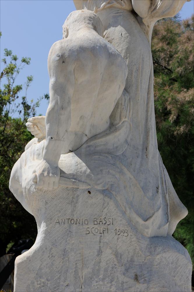 L'immagine esalta un bellissimo dettaglio del Monumento ai Caduti di Trani, dedicato ai concittadini caduti durante la Prima Guerra Mondiale. Il monumento a cippo fu realizzato nel 1923 da Antonio Bassi, scultore originario di Trani formatosi a Roma e Vienna. Tutto in pietra bianca di Trani, è collocato nella Villa Comunale, in prossimità del centro storico, un esempio affascinante di giardino all'italiana misto a giardino all'inglese che si affaccia sul mare. Il monumento è di tipo a cippo, sui cui basamenti sono evidenti alcuni bassorilievi e il bellissimo gruppo scultoreo, sempre in pietra locale, raffigurante l'Allegoria del sacrificio del soldato per la Patria.