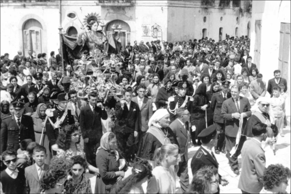 In questa foto storica il simulacro di San Primiano Martire è portato in processione per le vie del paese, accompagnato da una numerosa folla di devoti.
La festa patronale di San Primiano Martire è una celebrazione religiosa e popolare che si svolge ogni anno a Lesina (FG), dal 14 al 16 maggio. Al centro vi è il culto del santo, le cui reliquie giunsero a Lesina nel IX secolo da Larino, luogo del suo martirio nel 303 d.C.
Le celebrazioni comprendono la traslazione del simulacro alla Chiesa Madre, solenni funzioni liturgiche, la processione per le vie cittadine e la suggestiva processione sul Lago di Lesina, con la benedizione delle acque e dei pescatori.
Il culto si radicò a Lesina nel IX secolo, quando i monaci benedettini portarono qui le reliquie per salvarle dalle i...