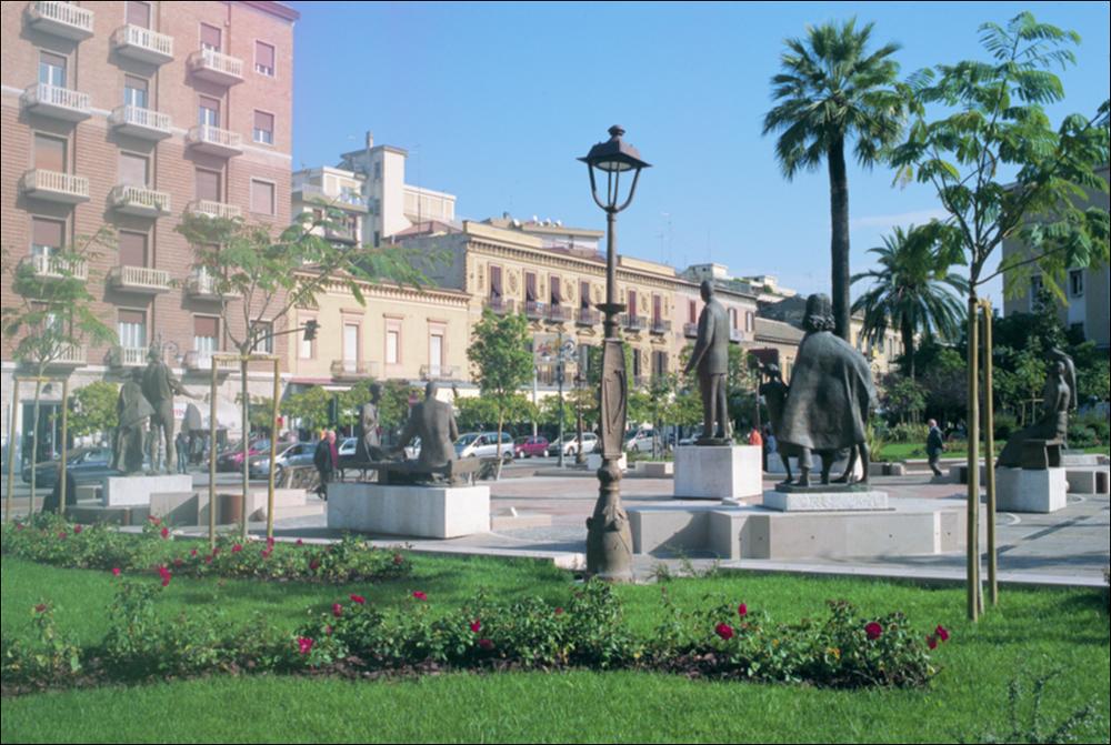 La fotografia è parte della ricca raccolta fotografica “Puglia per tutte le Stagioni” vol. 2, prodotta dall'Assessorato al Turismo e Industria Alberghiera della Regione Puglia e creata per raccontare la Puglia attraverso immagini diverse suddivise in 5 settori principali: Città e Paesi, Settimana Santa, Territorio, Feste – Sagre – Tradizioni, Mercati – Prodotti – Cucina. L'immagine immortala uno scorcio di Piazza Umberto Giordano, conosciuta anche come Largo di Gesù e Maria per via dell'omonima chiesa che vi si affaccia, a Foggia. Inizialmente, nel 1871, la piazza venne dedicata a Vincenzo Lanza, medico, politico e professore foggiano, con la sistemazione di una statua a lui dedicata. Successivamente, non avendo il Lanza giurato fedeltà al re una volta eletto deputato, ...