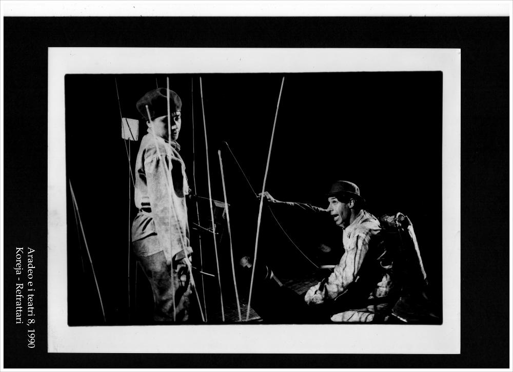 La fotografia in bianco e nero è un momento dello spettacolo "Refrattari", rappresentato nel 1990 dal Teatro Koreja durante l'ottava edizione di "Aradeo e i Teatri", un appuntamento con il teatro sperimentale che la compagnia nata nel 1983 nel piccolo borgo salentino di Aradeo porta avanti sin dall'anno della sua fondazione. Proposto per la prima volta proprio in quest'occasione, la rappresentazione teatrale diretta da Salvatore Tramacere è liberamente ispirata al "Woyzeck" di Georg Büchner e ai suoi personaggi. La sceneggiatura si basa sul concetto che i refrattari sono dei folli che vivono in un luogo chiuso, senza aria né luce. Metaforicamente vivono il vuoto in un mondo vicino al crollo, dove le certezze sono perse. L'unico modo per sentirsi vivi nel mondo è agitars...