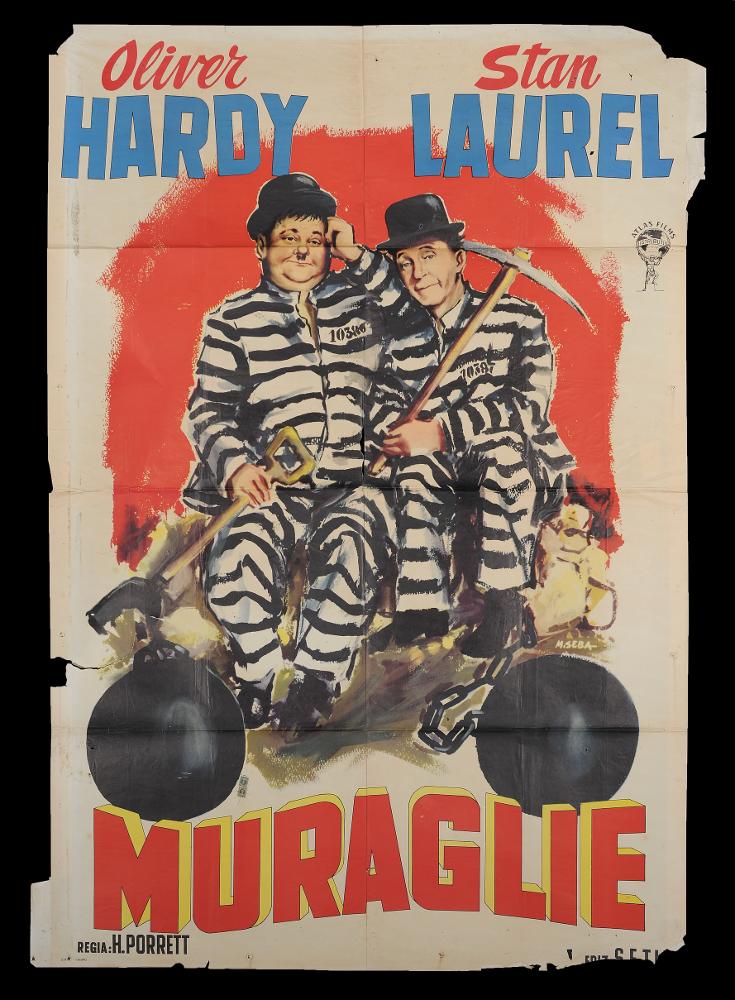 L'immagine riproduce uno dei manifesti conservati presso la Mediateca Regionale Pugliese (vedi Note). Si tratta del manifesto del film "Muraglie", a firma di M. Seba. È una delle moltissime composizioni realizzate per la comicità di Stanlio & Ollio, il duo iconico tra i più amati della storia del cinema. L'artista rivela uno stile narrativo moderno e composto in cui, su fondo rosso, spiccano i ritratti fedeli e realistici dei due attori in una composizione che risalta la comicità elementare della coppia artistica, nota al grande pubblico per le loro gag semplici ed esilaranti, adatte a ogni tipo di età. Le loro mimiche facciali, il linguaggio del loro corpo sono gli elementi di successo della loro arte comica....