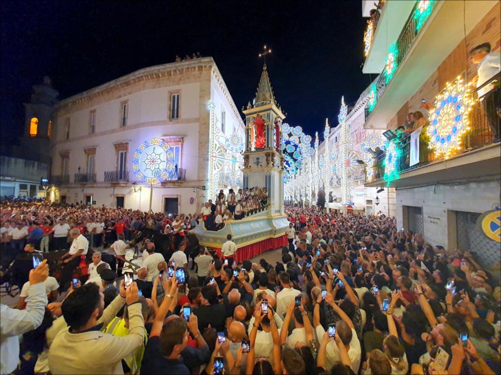 Lo scatto cattura l’arrivo del Carro Trionfale, attesissimo momento della Festa Patronale di Sant’Oronzo a Turi, accolto da un’esplosione di entusiasmo, gioia condivisa e profonda devozione popolare.
La Festa Patronale di Sant’Oronzo, che si celebra il 25 e 26 agosto, è molto più di una ricorrenza religiosa: è un intreccio di fede, tradizione e spettacolo capace, ogni anno, di coinvolgere l’intera comunità.
Simbolo indiscusso della festa è il maestoso Carro Trionfale: un’imponente torre lignea, trainata da sei mule, che riaccompagna il Santo dalla grotta fino al cuore del paese, tra giochi di luce, musica festosa e una folla gremita di emozione.
Il 25 agosto è dedicato alla Processione alla Grotta. Il busto di Sant’Oronzo parte dalla Chiesa Madre e viene accompagnato in...