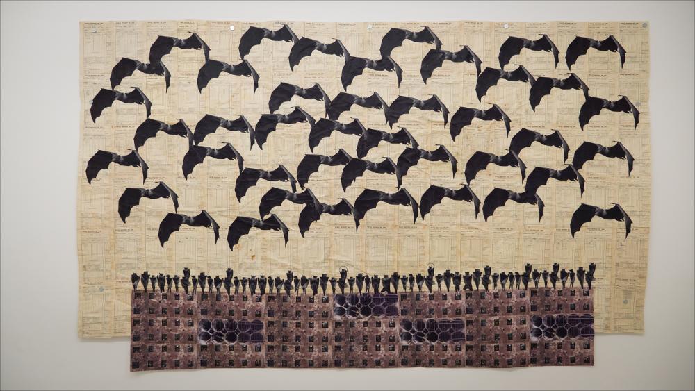 L’immagine presenta l’opera TINAMBANYI, 2020-2021, una delle opere di Ibrahim Mahami, vincitore del Premio Pascali 2021 (XXIII edizione), in mostra presso la Fondazione Museo Pino Pascali di Polignano a mare dall’11 dicembre 2021 al 13 marzo 2022.
L'opera fu realizzata da Mahama assemblando note d’archivio, disegni, fotografie a mappe dell’età coloniale, taccuini bancari e libri mastri degli anni Sessanta e Settanta. Questi documenti sono popolati da pipistrelli, animali che sono divenuti i protagonisti di una serie di collage. La presenza di questi animali è legata alla storia dell’acquisto, da parte di Mahama, di un silo industriale a Tamale, ribattezzato “Nkrumah Voli-ni”. Questo luogo, dopo l’abbandono nel 1966, vide al suo interno il sorgere di un ecosistema compos...