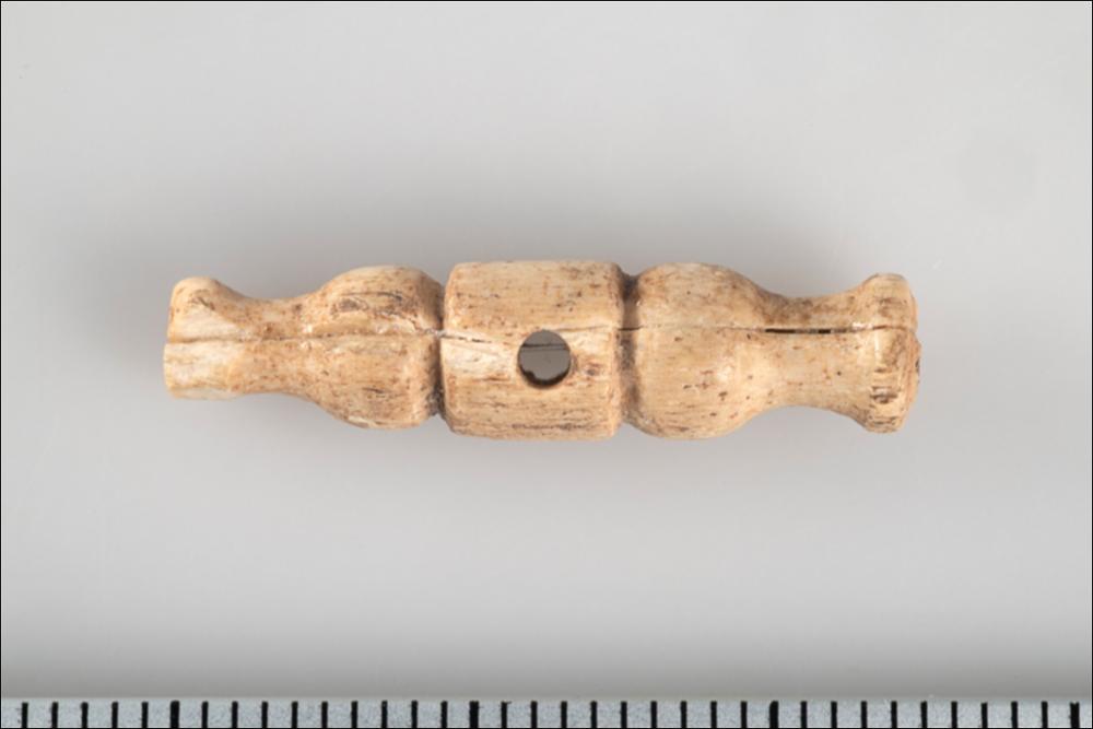 <div class="ql-editor"><div>Il piccolo ornamento in osso, proveniente dalla Grotta della Trinità, è caratterizzato da una parte centrale cilindrica e da due elementi laterali sagomati. Al centro presenta un foro, probabilmente utilizzato per fissare l’oggetto a un tessuto o a un indumento. Per questa caratteristica, il manufatto potrebbe essere stato impiegato come elemento decorativo del vestiario, forse con una funzione simile a quella di un bottone.</div></div>
