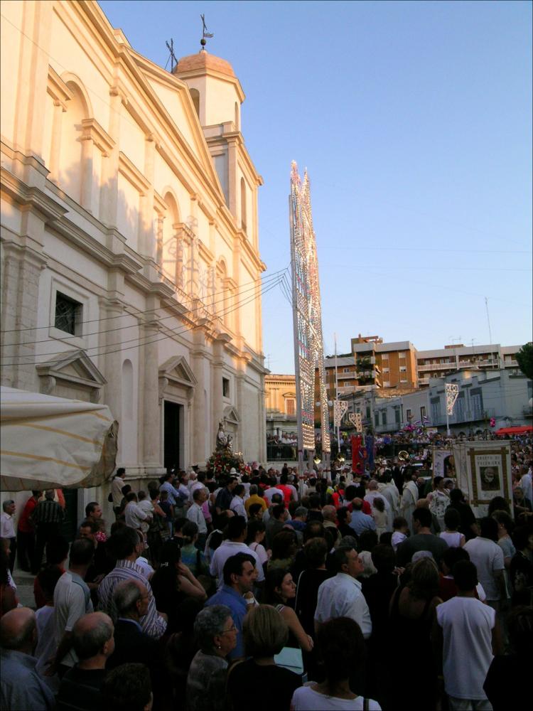 Fotografia storica della Processione di San Sabino, Canosa di Puglia, anno 1990.
Lo scatto ritrae la folla raccolta in piazza davanti alla Basilica, intenta a seguire il passaggio dei simboli della processione. Si distingue lo stendardo del Comune di Canosa, mentre dall’ingresso della Basilica di San Sabino emerge il busto argenteo del santo patrono, catturando un momento di devozione e partecipazione civica della comunità. <div><br>La festa patronale di San Sabino si celebra ogni anno il 1° agosto a Canosa di Puglia e rappresenta un momento centrale della vita culturale e religiosa della città. La ricorrenza rievoca la traslazione del corpo del santo dalla Basilica di San Pietro alla basilica a lui dedicata, un evento che unisce fede, storia e tradizione popolare.
La f...