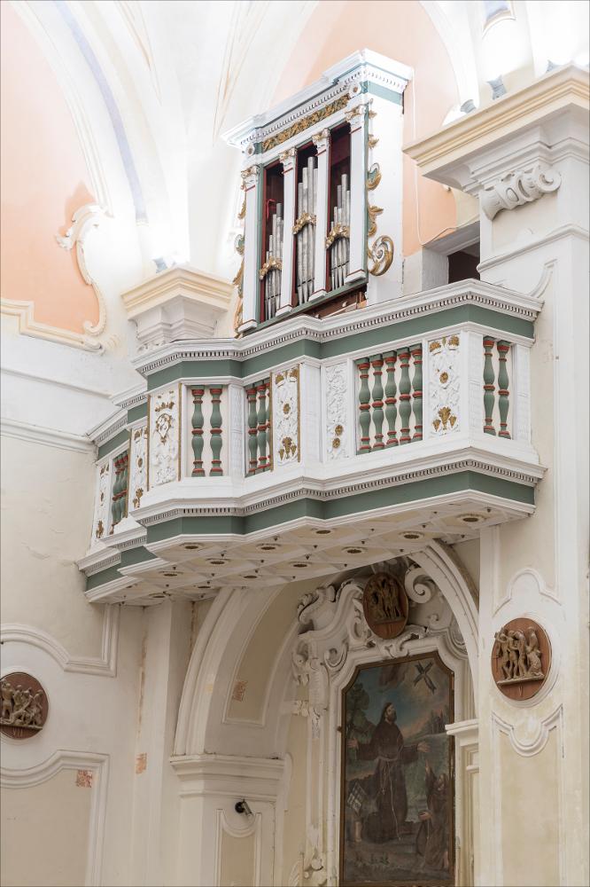 L'organo rappresentato nell'immagine digitale è collocato nella chiesa di S. Antonio di Minervino di Lecce. La chiesa fu costruita dall’Ordine dei Riformati di Lecce nel 1620 con l’annesso convento terminato nel 1628. La chiesa presenta una facciata molto semplice a due navate con un pregevole dipinto di Gian Domenico Catalano sull’altare maggiore e una scultura del Santo Antonio donata dall’arcivescovo de Andrada prima della sua morte nel 1628. L’organo è collocato in una piccola cantoria con una balaustra caratterizzata da pilastrini intagliati e pannelli decorativi con stilemi floreali, al centro uno scudo con un’aquila a doppia testa. La cassa d’organo datata 1733 risulta il primo lavoro dell’organaro e si presenta molto semplice con un profilo piatto suddiviso da q...