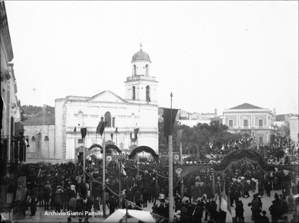 Fotografia storica del 1933. Scatto recuperato e digitalizzato dall’Archivio Gianni Pansini, mostra la facciata della Basilica di San Sabino con la piazza allestita a festa con stendardi e bandiere. La folla numerosa, girata di spalle verso la basilica, osserva il passaggio dei simulacri durante la processione patronale, catturando un momento di intensa partecipazione collettiva.
<div><br>La festa patronale di San Sabino si celebra ogni anno il 1° agosto a Canosa di Puglia e rappresenta un momento centrale della vita culturale e religiosa della città. La ricorrenza rievoca la traslazione del corpo del santo dalla Basilica di San Pietro alla basilica a lui dedicata, un evento che unisce fede, storia e tradizione popolare.
La festa è caratterizzata da un forte coinvolgime...