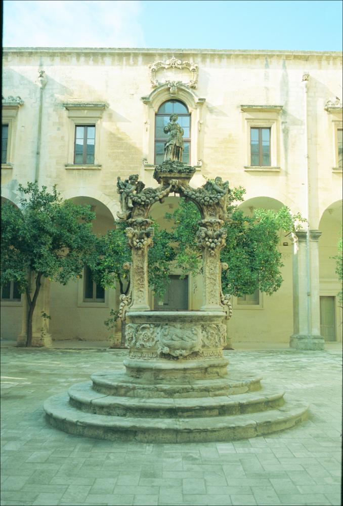 La fotografia è parte della ricca raccolta fotografica “Puglia per tutte le Stagioni” vol. 2, prodotta dall'Assessorato al Turismo e Industria Alberghiera della Regione Puglia e creata per raccontare la Puglia attraverso immagini diverse suddivise in 5 settori principali: Città e Paesi, Settimana Santa, Territorio, Feste – Sagre – Tradizioni, Mercati – Prodotti – Cucina. L'immagine immortala il pozzo, conosciuto come “Vera Ovale”, all'interno del giardino che circonda il Palazzo del Seminario di Lecce. Il manufatto è stato realizzato nel 1707 dall'architetto Giuseppe Cino ed è singolarmente rappresentato come un canestro di frutta con manico, adornato con ramoscelli e foglie di pietra della specie mediterranea dell'acanthus spinosus, raspi d'uva, sormontato in alto da u...