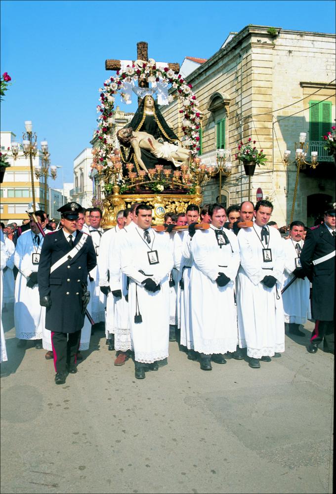 La fotografia è parte della ricca raccolta fotografica “Puglia per tutte le Stagioni” vol. 2, prodotta dall'Assessorato al Turismo e Industria Alberghiera della Regione Puglia e creata per raccontare la Puglia attraverso immagini diverse suddivise in 5 settori principali: Città e Paesi, Settimana Santa, Territorio, Feste – Sagre – Tradizioni, Mercati – Prodotti – Cucina. L'immagine digitale mostra la processione della “Pietà” a Ruvo di Puglia, l'ultima in chiusura dei riti penitenziali della Settimana Santa. La processione ha inizio per le 16:30 del Sabato Santo, quando il simulacro della Madonna fa la sua uscita dalla chiesa del Purgatorio sollevata dai confratelli vestiti di camice bianco con la tracolla nera, su cui spicca il medaglione argenteo, con un teschio e gli...