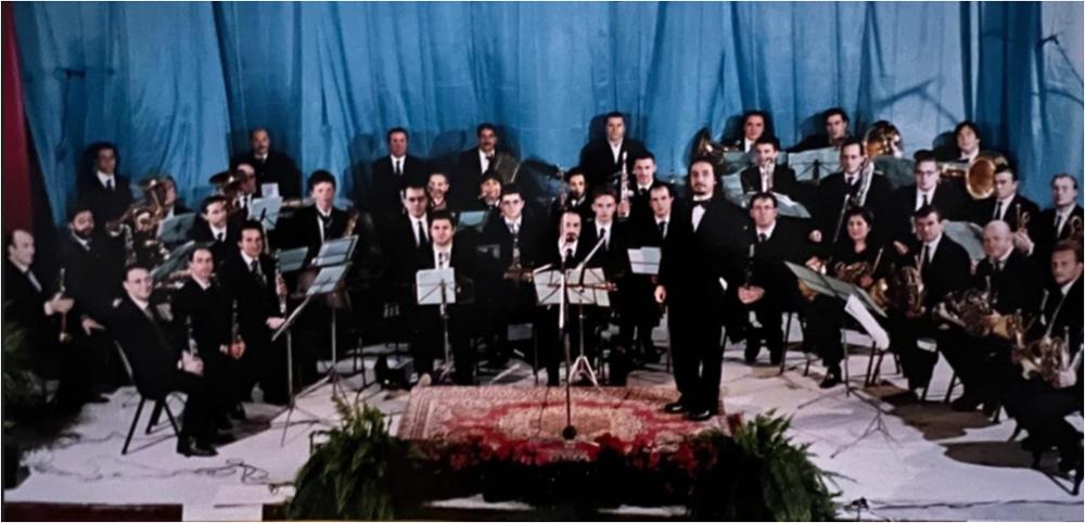<div class="ql-editor"><div>Fotografia che ritrae la formazione della Banda Musicale G. Verdi di Canosa di Puglia durante il concerto in occasione della festa di Santa Cecilia, svoltosi nel 1998 presso il Teatro Comunale di Canosa di Puglia.</div><div><br></div><div>La Banda Musicale G. Verdi di Canosa di Puglia affonda le proprie origini nel 1861, anno in cui l’istituzione della Banda Municipale è documentata nell’Archivio Decurionale del Comune di Canosa attraverso il primo contratto stipulato con il maestro Antonio Tonti. Nel corso della sua lunga storia, la banda ha mantenuto un rapporto continuativo con l’Amministrazione comunale e con la comunità cittadina, consolidando il proprio ruolo nella vita culturale e musicale del territorio. La...