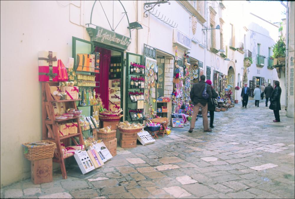 La fotografia è parte della ricca raccolta fotografica “Puglia per tutte le Stagioni” vol. 2, prodotta dall'Assessorato al Turismo e Industria Alberghiera della Regione Puglia e creata per raccontare la Puglia attraverso immagini diverse suddivise in 5 settori principali: Città e Paesi, Settimana Santa, Territorio, Feste – Sagre – Tradizioni, Mercati – Prodotti – Cucina. L'immagine immortala un particolare del centro storico di Otranto, comune della provincia di Lecce in Puglia. Otranto ha vissuto più vite: prima centro greco-messapico e romano, poi bizantino e più tardi aragonese, si sviluppa attorno all'imponente castello e alla cattedrale normanna. Sede arcivescovile e rilevante centro turistico, ha dato il suo nome al Canale d'Otranto, che separa l'Italia dall'Alban...