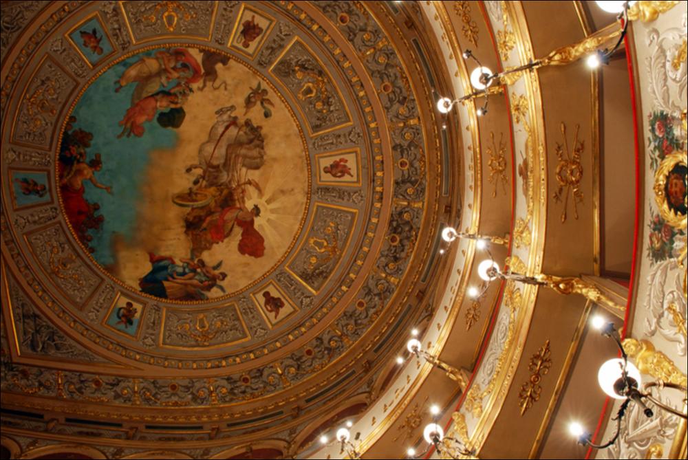L'immagine è parte della campagna fotografica realizzata dalla fotografa Margherita Mirabella per Teatro Pubblico Pugliese, che con i suoi scatti ha ripreso le eleganti architetture e i rifiniti dettagli di alcuni dei più bei teatri pugliesi e di alcuni spettacoli teatrali portati in scena in questi ultimi anni. Lo scatto immortala con una bella prospettiva dal basso l'affresco posto sul soffitto di Teatro Curci di Barletta, opera del pittore barlettano Giambattista Calò, artista di scuola napoletana ottocentesca, che fu maestro di De Nittis e di una intera generazione di pittori. Era molto apprezzato dalla sua città, tanto che "la morte improvvisa di questo valoroso artista, di questo tipo d'insegnante e di gentiluomo, avvenuta il giorno 28 agosto (1895), fu dolore viv...